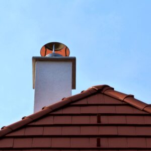 a white stucco chimney on a red roof with a metal chimney cap