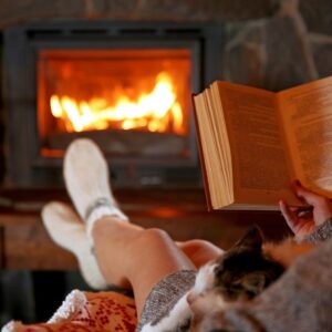 a person wearing socks and reading a book by a cozy fireplace