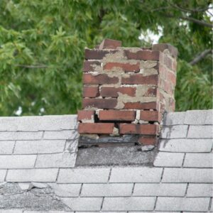 a chimney with damaged masonry on a gray roof