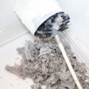 a white vent-cleaning brush coming out of a vent surrounding by gray lint