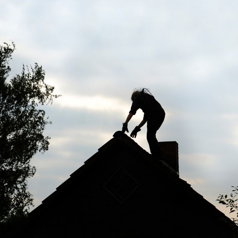 a silhouette of a chimney technician on a roof by a chimney