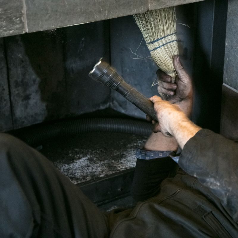 a chimney technician shining a flashlight into a chimney from the firebox while holding a chimney broom