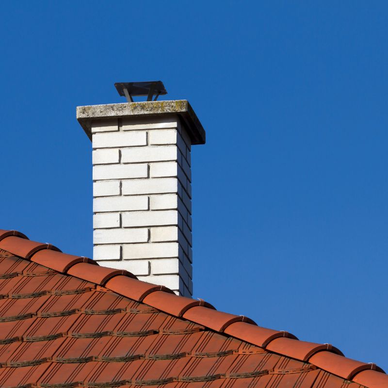 a white brick chimney coming off a red roof with a blue sky in the background